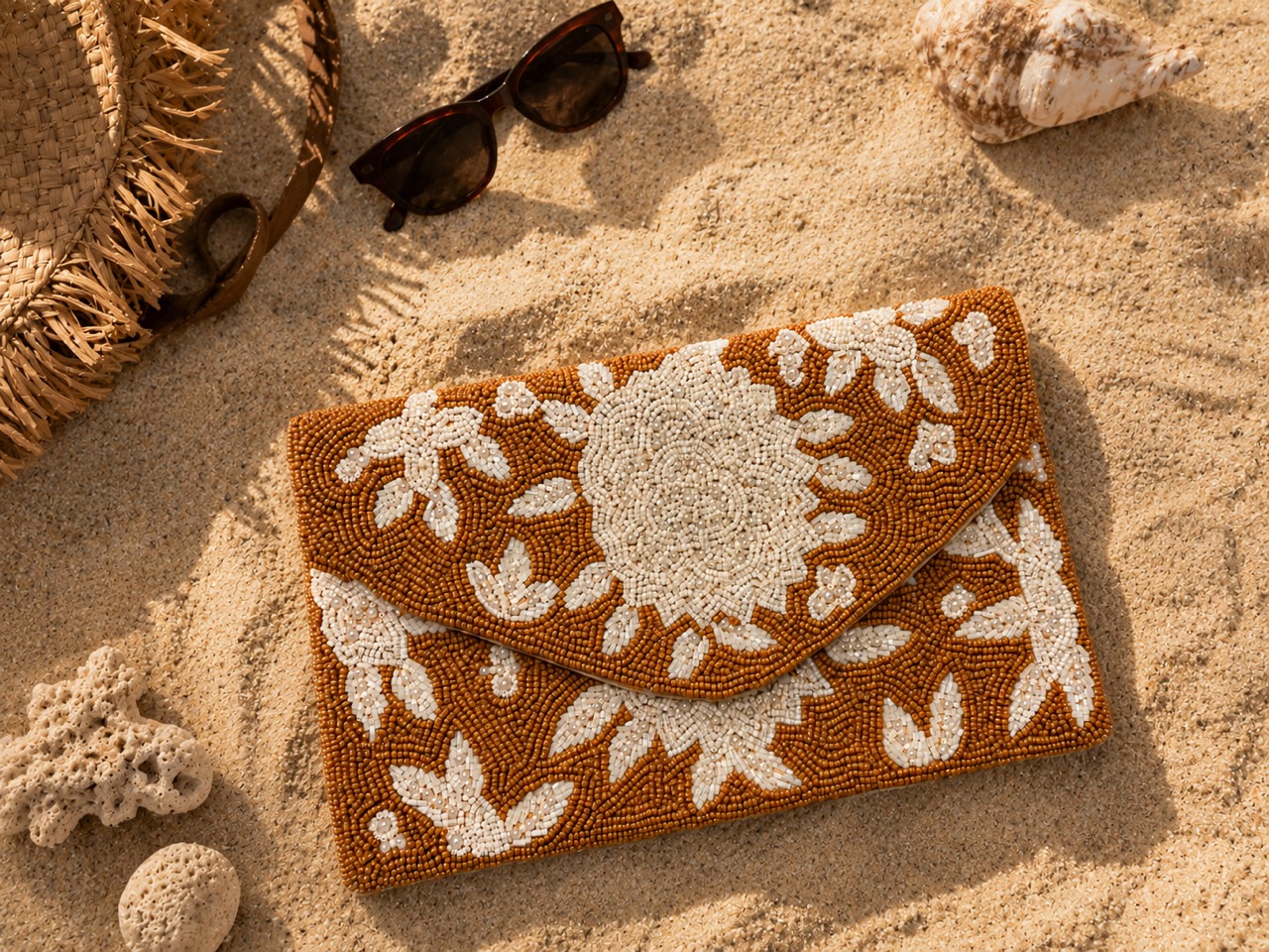 Bolso de cuentas en tonos terracota sobre arena junto a unas gafas de sol