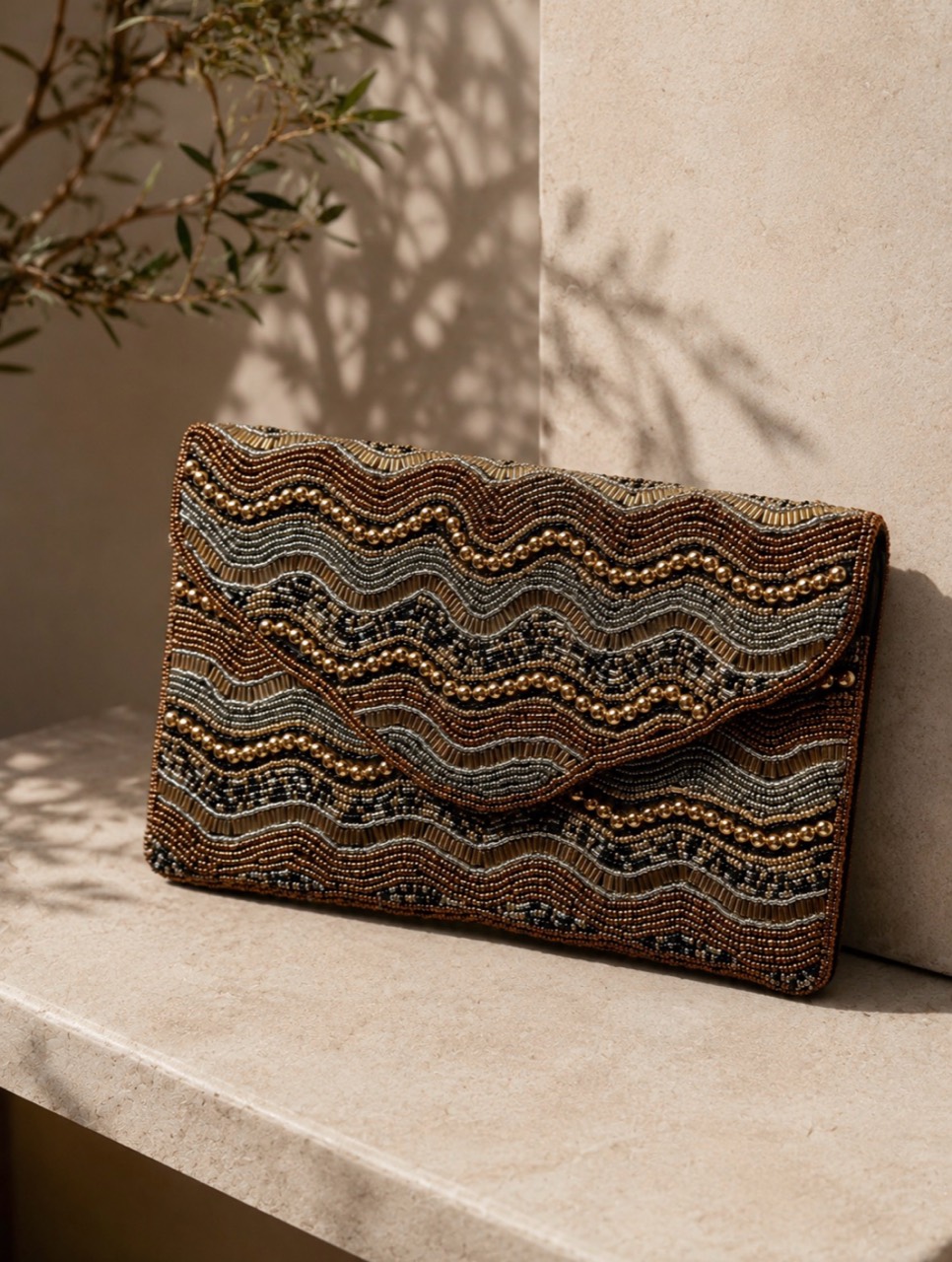 Clutch bordado en tonos chocolate y dorado sobre una superficie de piedra
