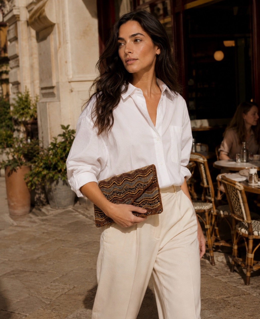 Mujer con camisa blanca y bolso de mano estampado en una calle mediterránea